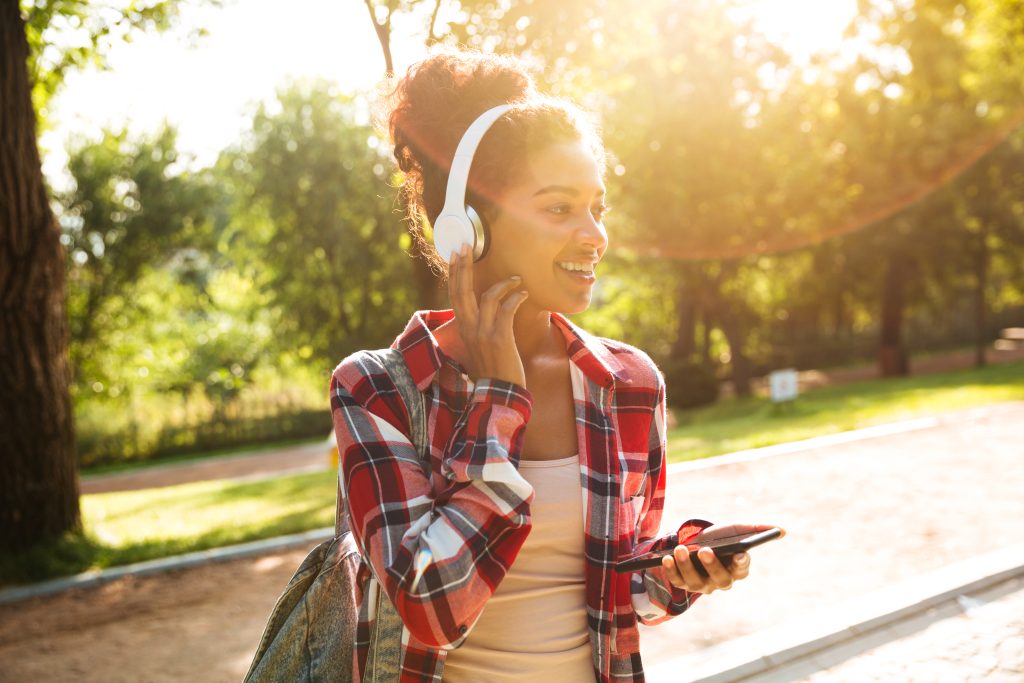 Mulher sorridente com fones de ouvido e smartphone, caminhando em um parque sob a luz do sol, simbolizando o crescimento do streaming e as oportunidades para o marketing digital.